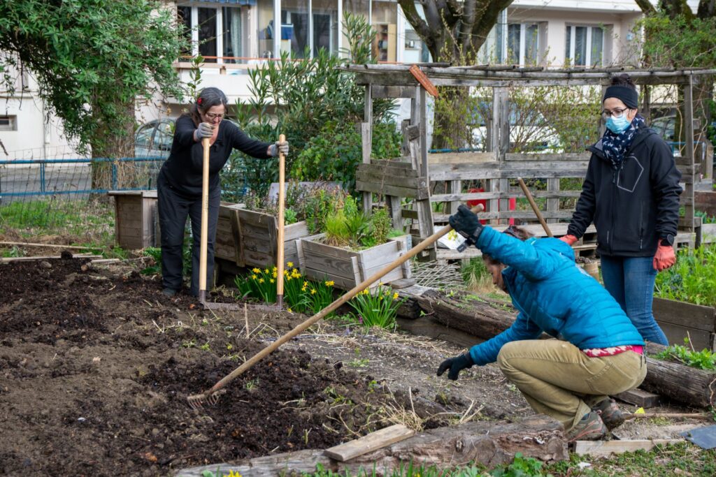 Trois personnes travaillent la terre dans un jardin partagé